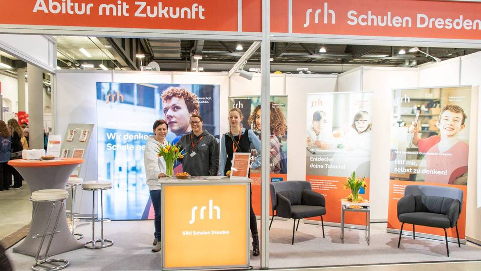 Ein Messestand mit dem Namen "jrh Schulen Dresden" mit mehreren Personen und Informationsmaterialien.