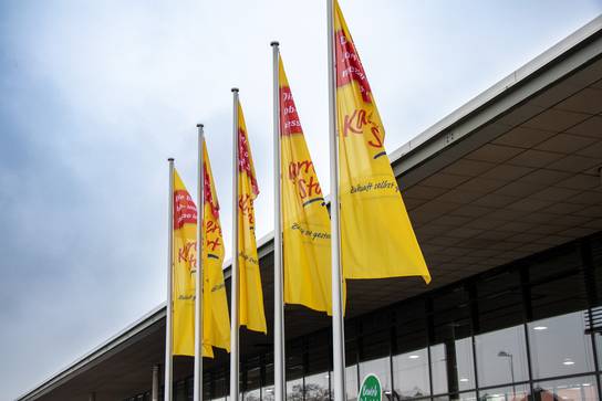 Mehrere gelbe Flaggen mit rotem Text vor einem Gebäude.