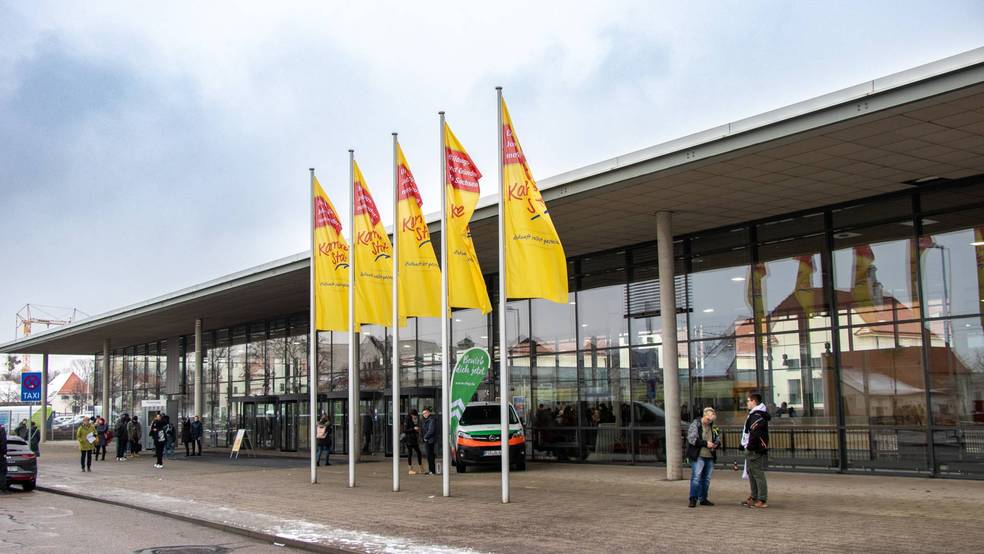 Ein Gebäude mit mehreren gelben und roten Fahnen vorne, Menschen gehen ein und aus.