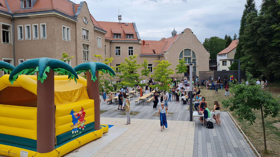 Außenveranstaltung mit aufblasbarem Spielplatz und Menschen, die sich auf einem Hof versammelt sind.