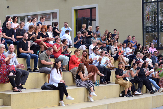 Große Gruppe von Menschen sitzt auf Stufen vor einem Gebäude.
