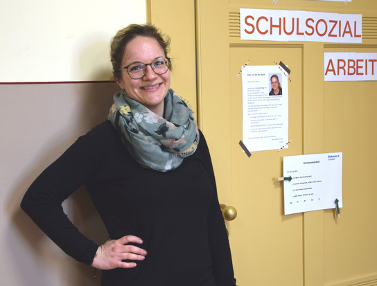 Eine Frau steht vor einer gelben Tür mit Anschlägen.