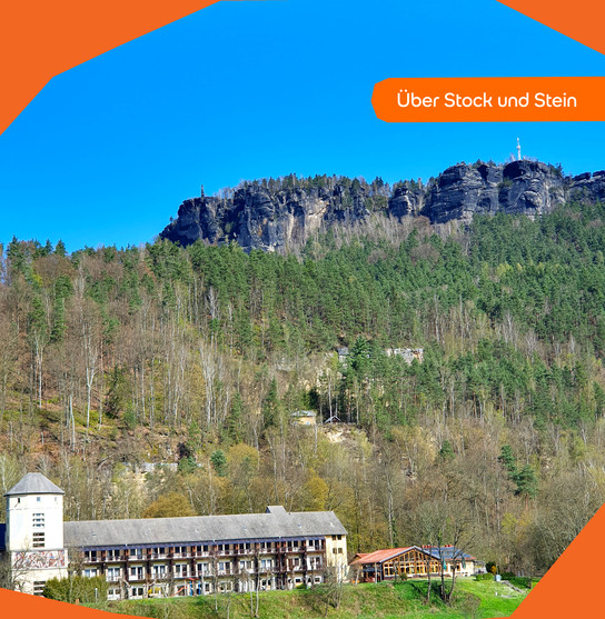 Ein Gebäude vor einem bewaldeten Berg mit einem Felsvorsprung und klarem blauem Himmel.
